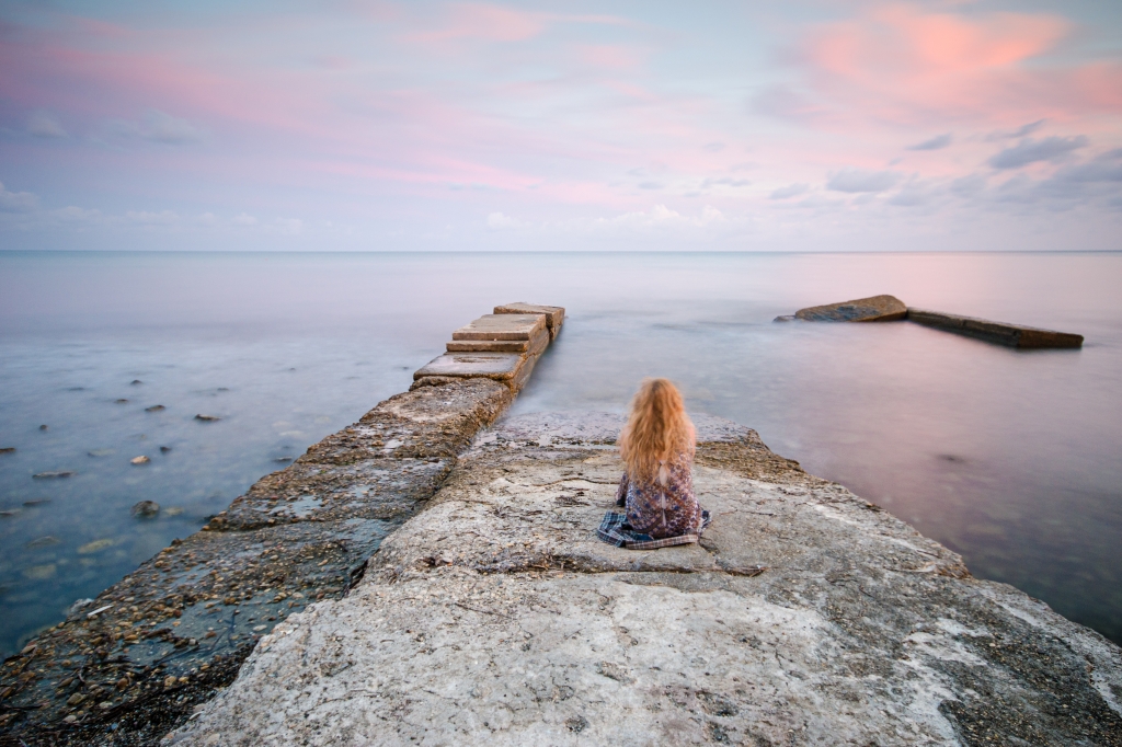 Una ragazza solitaria guarda il mare calmo al tramonto rosa
