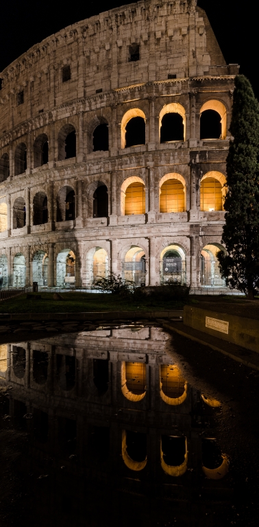 Il Colosseo di notte si riflette maestoso in una pozzanghera