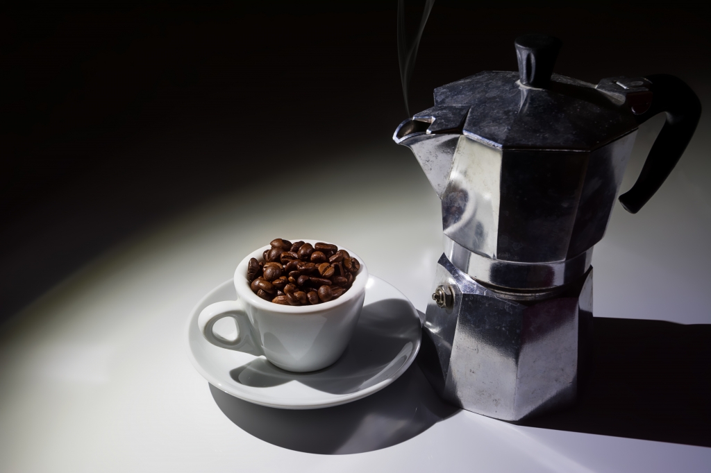 Tazzina per caffé piena di chicchi di caffé e caffettiera moka