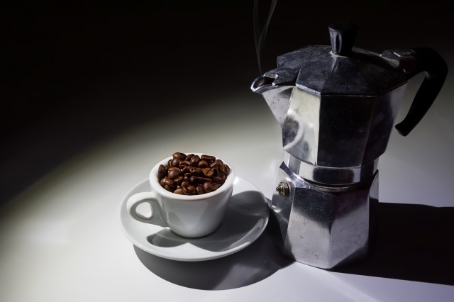 Tazzina per caffé piena di chicchi di caffé e caffettiera moka