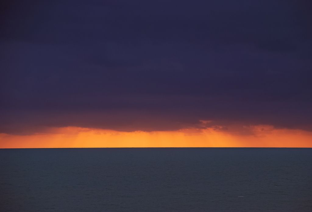 Tramonto su mare calmo con nuvole basse sull'orizzonte