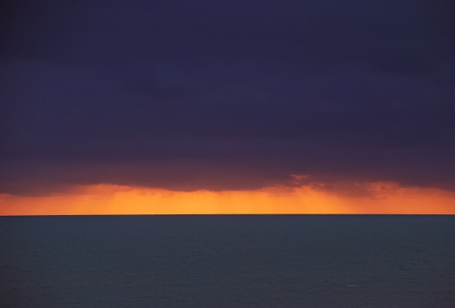 Tramonto su mare calmo con nuvole basse sull'orizzonte